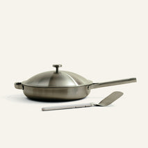 Stainless steel frying pan with lid and spatula on a white background